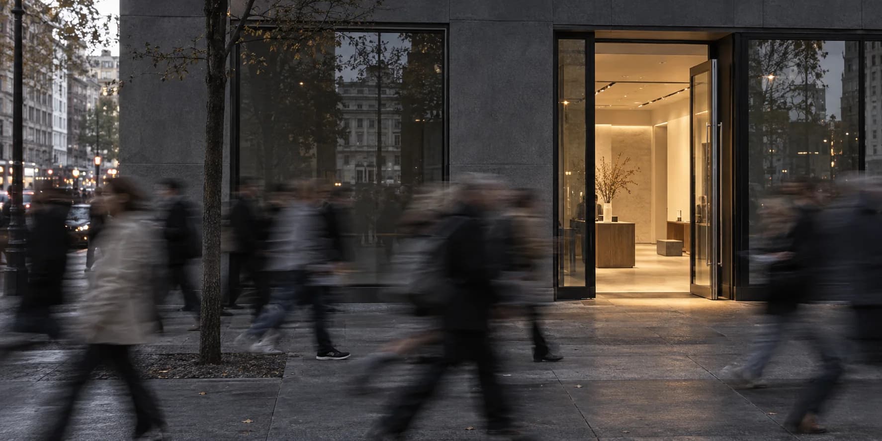 Pedestrians blur past an open, warmly lit shop while nobody walks in